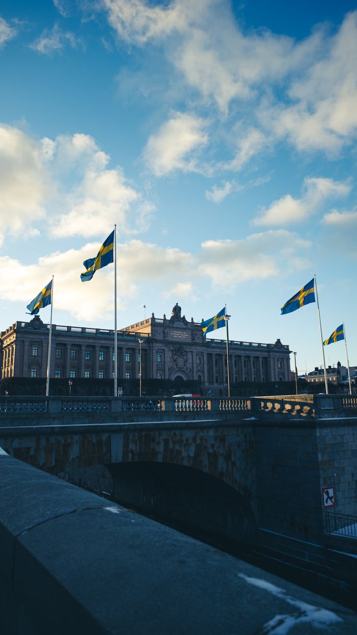 The Swedish Parliament building in Stockholm with flags flying under a clear blue sky.